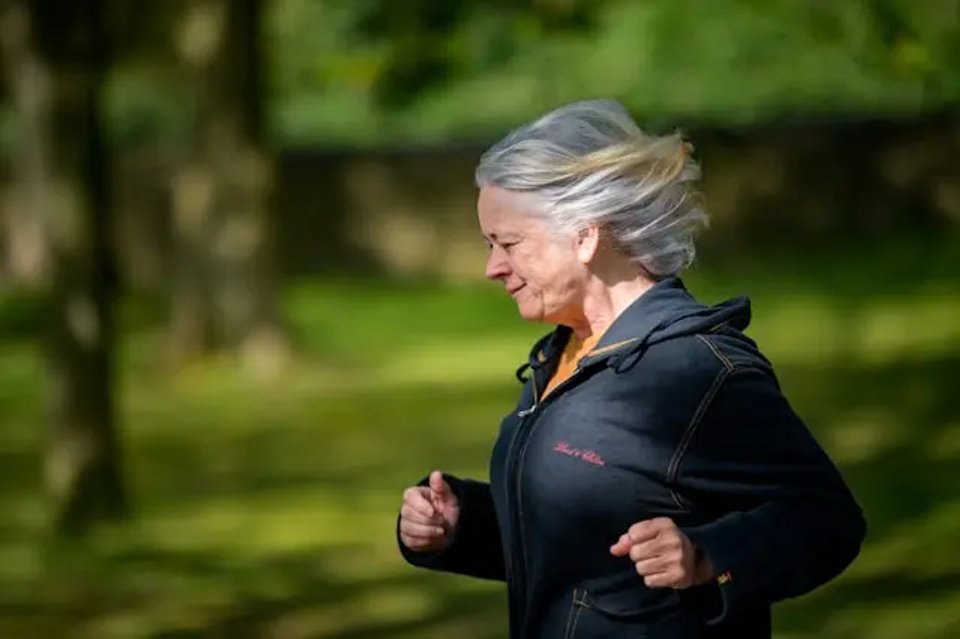 An active senior woman jogging in a park, enjoying the outdoors with her hair flowing in the breeze.