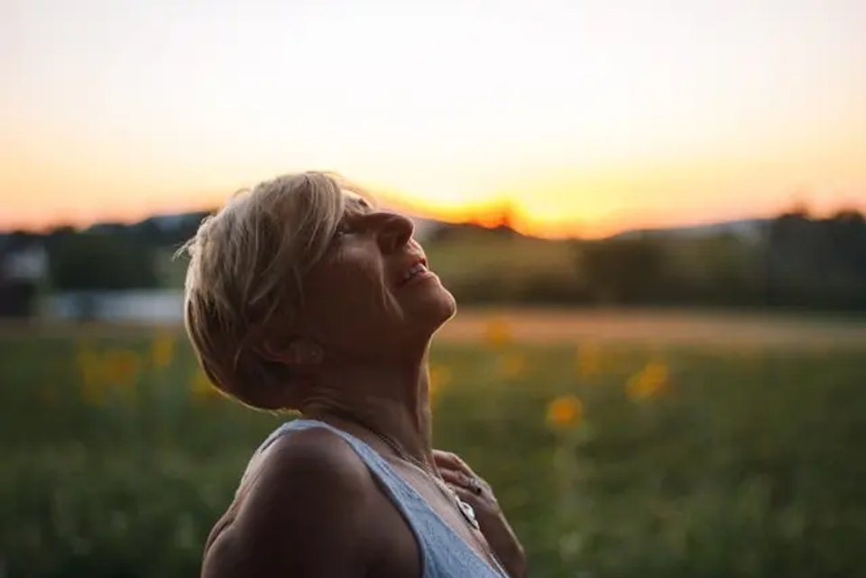 A woman with short blonde hair gazes upward, enjoying a sunset in a field filled with flowers.
