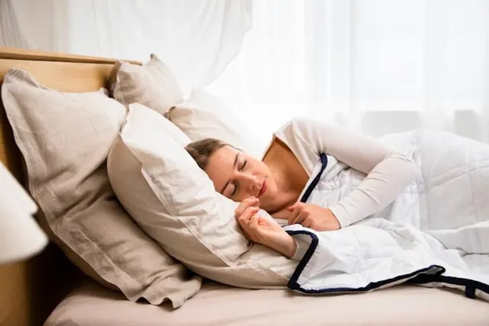 A woman peacefully sleeping in a cozy bed surrounded by soft pillows and a warm blanket, with natural light filtering through the window.